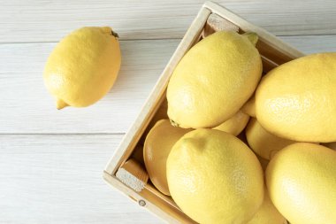 Tahta bir kutuda olgun limonlar. Beyaz ahşap arka planda taze limonlar. Üst Manzara. Olgun ve lezzetli narenciye meyvesi. Metin için alanı kopyala.