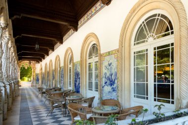 Süslü sütunları olan Portico, geleneksel Azuleju fayansları olan galeri, Portekiz Bussaco Sarayı 'ndaki ahşap tavan ve mermer zemin. Turistler dinlensin diye otelin girişindeki masalar, sandalyeler.