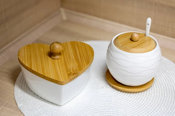 White ceramic sugar bowl and candy bowl with wooden lids on a kitchen table. Selective focus