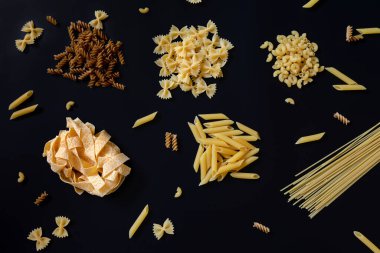 Siyah arka planda farklı türde kurutulmamış makarna. Çiğ pappardelle, penne, spagetti, farfalle ve fusilli. İtalyan makarna pişirme konsepti.