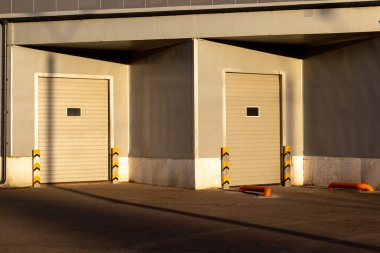 Gün batımında iki beyaz metal kapılı, endüstriyel gri depo cephesi.