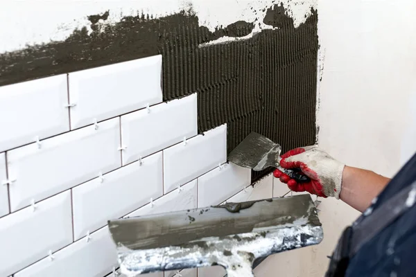 Wall cladding. The master\'s hands apply tile glue to the walls using two spatulas or trowels of different sizes. Selective focus