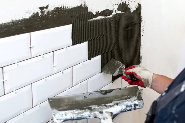 墙壁熔覆 主人的手在墙壁上涂瓷砖胶水 使用两种不同尺寸的水沫或焊条 有选择的重点 图库图片