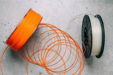 3D Yazıcı Plastik Filamanlar. 3D baskı için turuncu ve beyaz termoplastik kablolar gri taş zemin üzerine yakın, düz yatıyordu