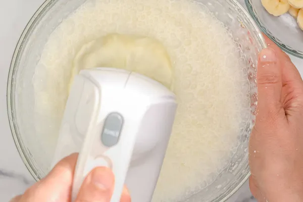 Whipped cream cheese desert recipe. Mixing ingredients in a glass bowl using an electric mixer, close up cooking process, woman hands