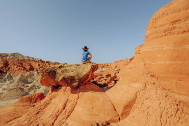 Büyük bir kayanın üzerinde oturan, çölde yürüyüş yapan bir kadın silueti. Grand Staircase-Escalante Ulusal Anıtı, Utah.