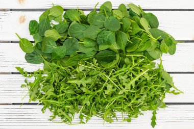 Baby spinach and arugula green leaves close up on white wooden background, copy space