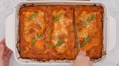 Mutfak masasına yakın fırında ıspanaklı lazanya. Kadın dilimlerle lazanya kesiyor..