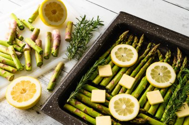 Taze yeşil kuşkonmaz, dilimlenmiş limon ve tereyağı, taze biberiye ve mevsimlik. Pişirilmeye hazır, fırında pişirilmeye hazır.