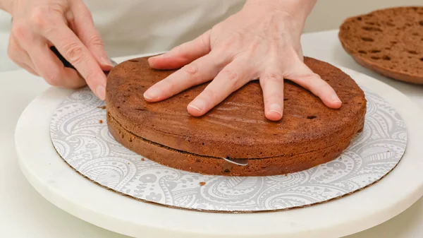 Chocolate cake step by step recipe. Woman hands slicing fresh baked cake into layer using a knife. Close up baking process