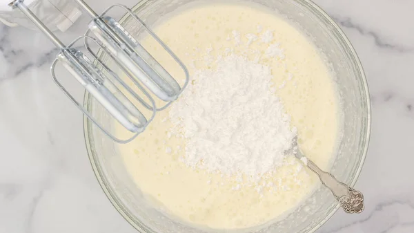 Cream cheese, milk cream and powdered sugar in a glass bowl. Mixing ingredients together using an electric mixer, flat lay, marble background, copy space