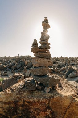 Güneş batarken güneşli bir kayalık sahilde deniz taşları piramidi. Yaşam dengesi ve uyum konsepti, dikey bayrak