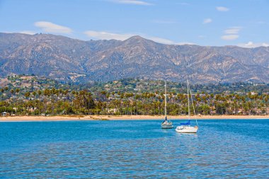 Santa Barbara harbor, California. Boat on a water, beautiful beach with palm trees, and mountains on a horizon