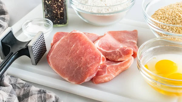 Breaded pork chops recipe. Ingredients close up on kitchen table. Raw pork chops, eggs, flour, bread crumbs, salt and black pepper