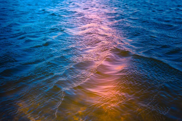 Abstract water background. Water surface and sun reflection. Beautiful blue, turquoise, orange, and pink colors