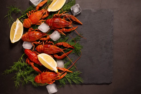 Kaynamış kırmızı kerevit, limon dilimleri ve siyah bir yüzey üzerinde buz küpleriyle yemeye hazır..