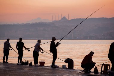 İstanbul, Türkiye 'de güneş ışığına karşı İstanbul Boğazı' nda balık tutan Balıkçıların siluetleri.