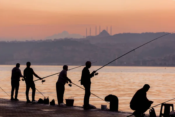 İstanbul, Türkiye 'de güneş ışığına karşı İstanbul Boğazı' nda balık tutan Balıkçıların siluetleri. — Stok fotoğraf