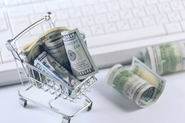 Bulanık bilgisayar klavyesine karşı bir alışveriş arabasındaki dolar parası. Çevrimiçi iş kavramı. — Stok fotoğraf