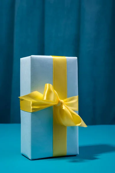 Caja de regalo con lazo amarillo contra fondo azul negrita y cortina. —  Fotos de Stock