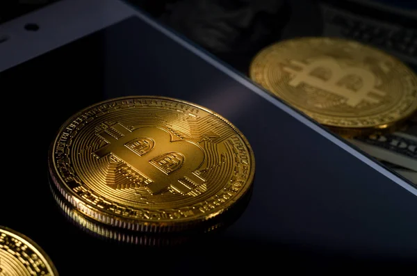 Oro físico Bitcoin Moneda contra billetes de dólar y teléfono inteligente sobre un fondo morado . — Foto de Stock
