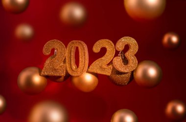 New Year banner with golden sparkling number 2023 and christmas balls against dark red color background.
