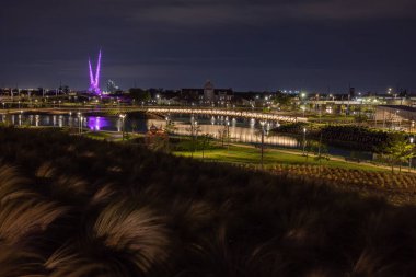 Oklahoma City, Oklahoma, ABD - 15 Nisan 2021: Arka planda yapay nehir ve soyut heykel bulunan gece makas kuyruğu parkı