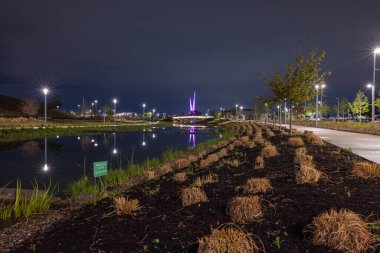 Oklahoma City, Oklahoma, ABD - 15 Nisan 2021: Arka planda yapay nehir ve soyut heykel bulunan gece makas kuyruğu parkı