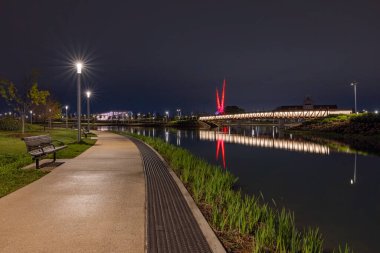 Oklahoma City, Oklahoma, ABD - 15 Nisan 2021: Arka planda yapay nehir ve soyut heykel bulunan gece makas kuyruğu parkı
