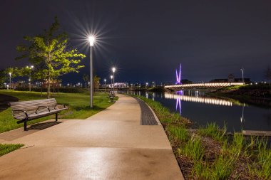 Oklahoma City, Oklahoma, ABD - 15 Nisan 2021: Arka planda yapay nehir ve soyut heykel bulunan gece makas kuyruğu parkı