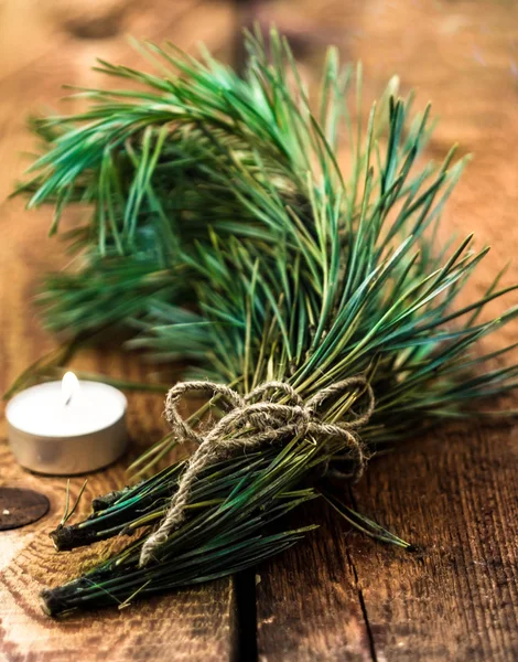 Bunch of fir tree or pine branches and glowing candle on dark old background. — Stock Photo, Image
