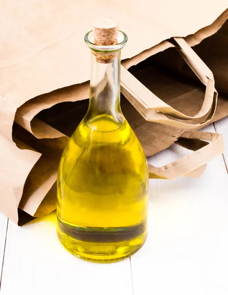 Bottiglia di olio d'oliva e sacchetto di carta su sfondo di legno bianco . — Foto Stock
