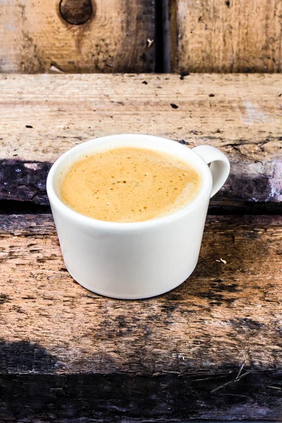 Cappuccino-Kaffeetasse mit Schaum auf weißem Untersetzer auf altem dunklem Holz. — Stockfoto