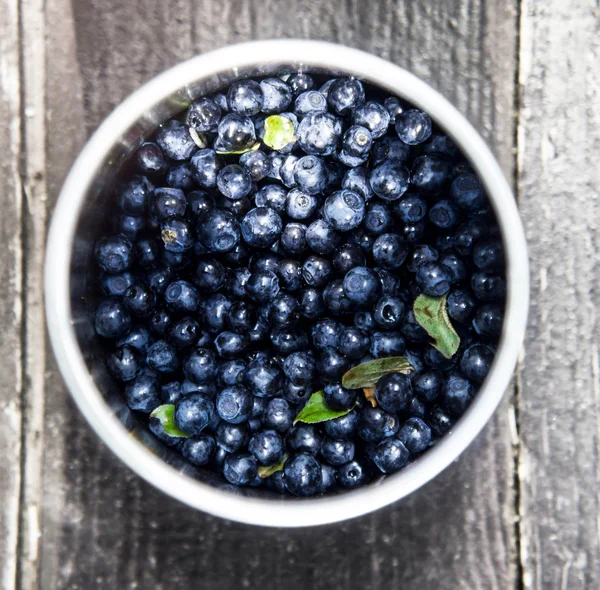 Blaubeeren in einer Schüssel mit Blättern auf rustikalem Hintergrund. — Stockfoto