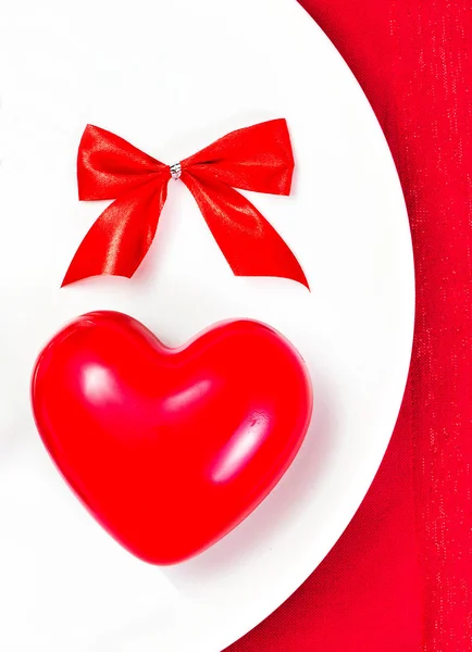 Red Heart on a white plate plate on festive napkin with red bow. — Stock Photo, Image