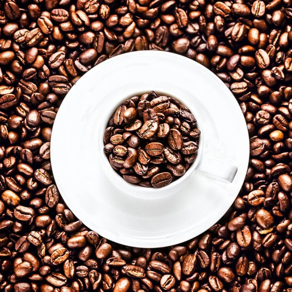 Taça de café branco com pires cheios de grãos de café torrados — Fotografia de Stock