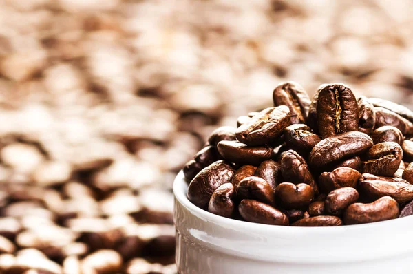 Taça branca cheia de grãos de café torrados em montes de grãos de café — Fotografia de Stock