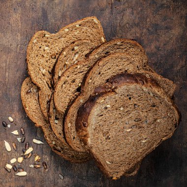 Pieces of wholegrain bread on dark ructic wooden background closeup. Freshly baked sourdough bread with seeds and crumbs.