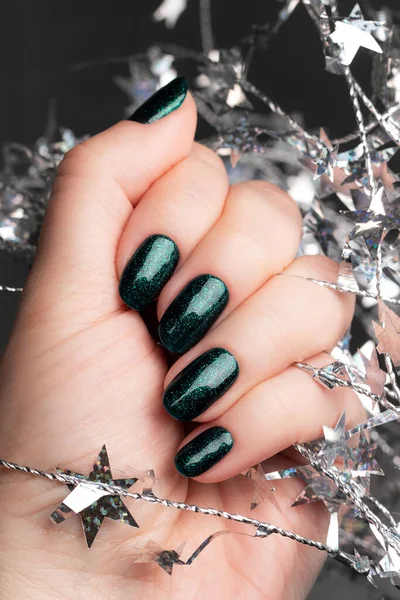 Hand met groene glitternagels met kerstslinger — Stockfoto
