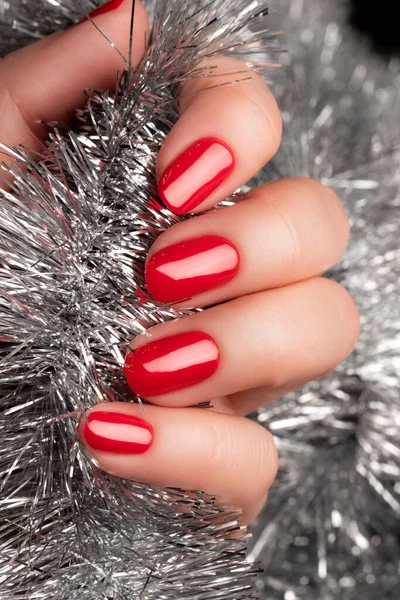 Рука с красными ногтями с рождественской мишурой — стоковое фото