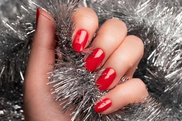 Hand with red nails with Christmas tinsel — Stock Photo, Image
