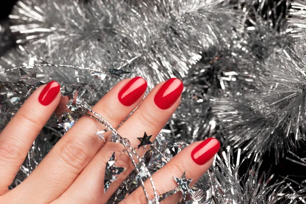 Рука с красными ногтями с рождественской мишурой — стоковое фото