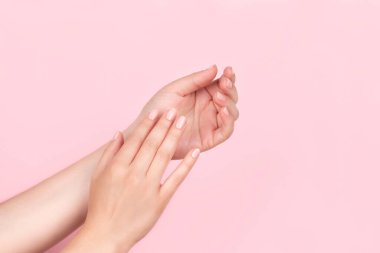 Güzel doğal manikürlü kadın elleri pembe arka planda pembe çıplak tırnaklar. Çivi bakımı kavramı