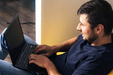 Laptopta çalışan yakışıklı sakallı adam ve modern ofiste sarı fasulye çuvalının üzerinde oturan yumuşak koltuk.