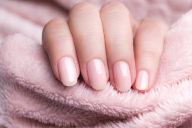 Güzel doğal manikürlü bir kadın eli. Soluk pembe tüylü kumaş üzerinde pembe çıplak tırnaklar. Tekstil arka planı.