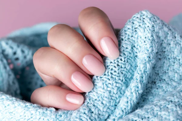 Female hand in blue knitted sweater with beautiful natural manicure - pink nude nails. Nail care concept