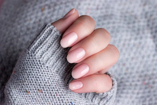 Female hand in gray knitted sweater with beautiful natural manicure - pink nude nails. Nail care concept