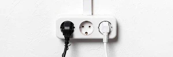 Group of white european electrical outlets with two plugs inserted into it on white concrete wall with copy space banner. Wide panoramic header