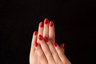 Female hands with beautiful manicure - red nails on dark black background. Nail care concept
