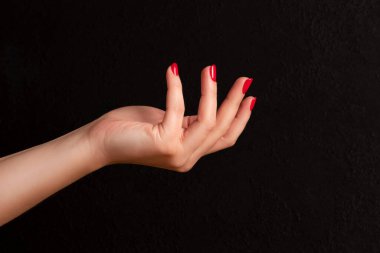 Female hand with beautiful manicure - red nails on dark black background. Nail care concept